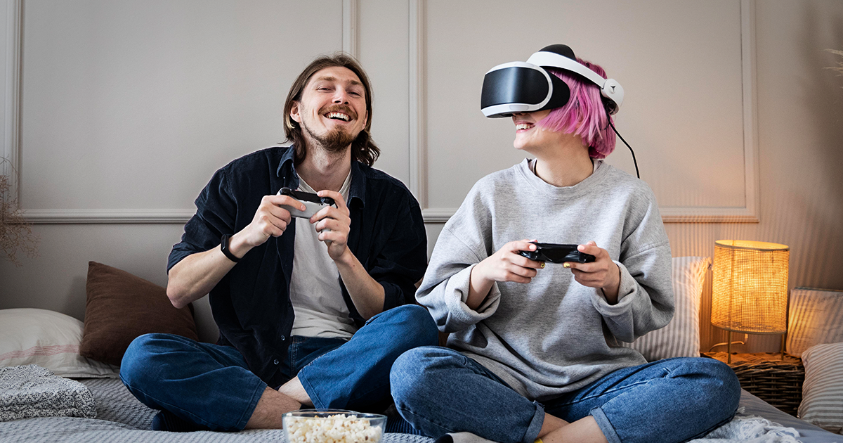 Dos personas sonriendo usando consolas de videojuego y lentes de realidad virtual.